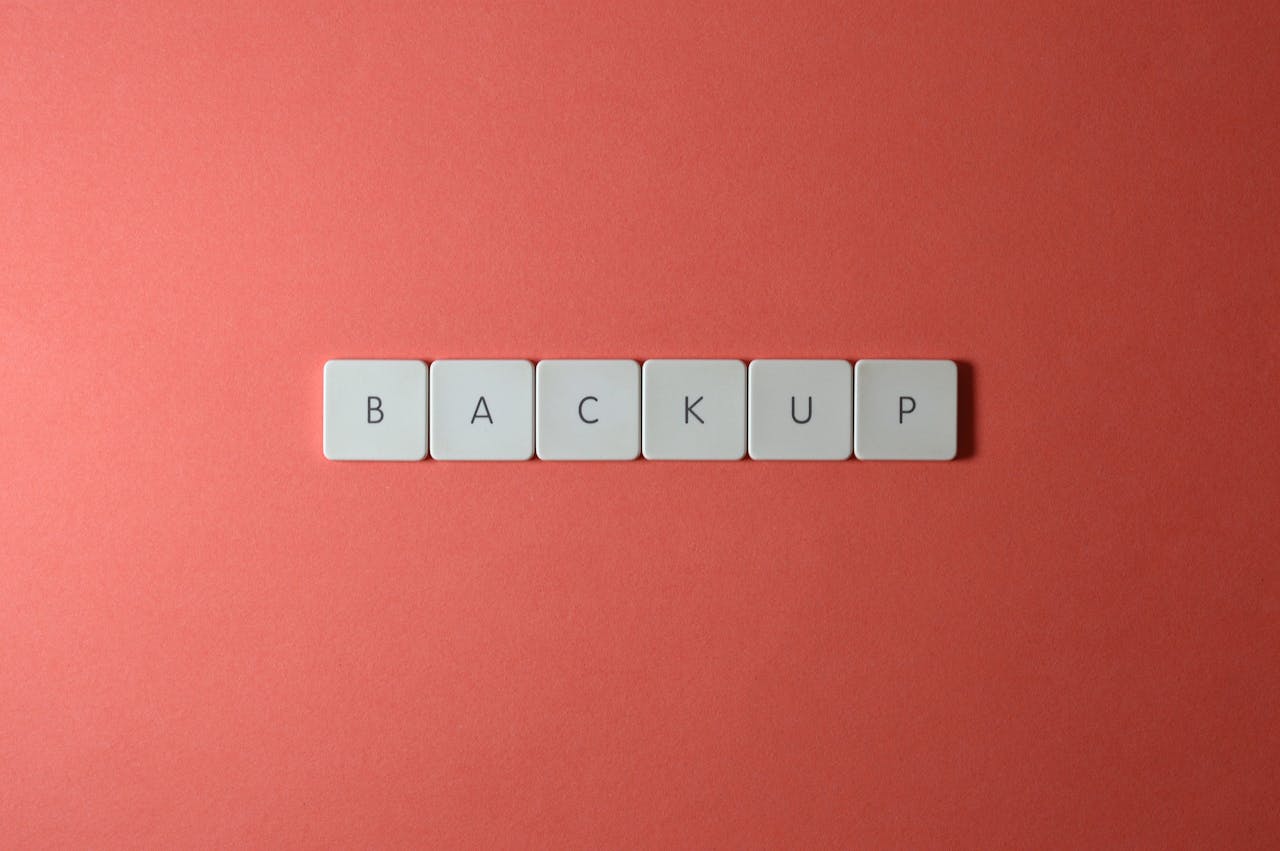Close-up of keyboard keys spelling BACKUP placed on a coral-colored surface.